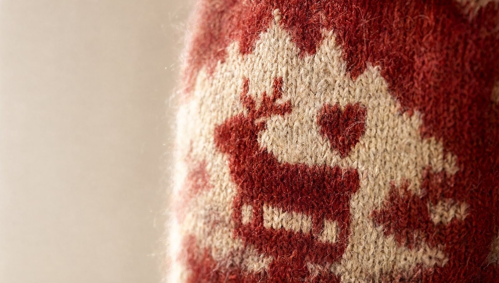 Close-up of cranberry and cream Fair Isle knitting with a small reindeer and heart